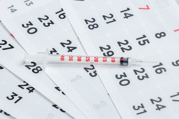 Syringe on a monthly calendar close-up. Vaccination