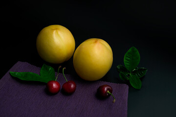 Two yellow peaches and cherries on a purple table cloth