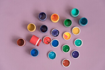 Open jars with gouache on a pink background. The view from the top. Variety of colors. Background, texture.