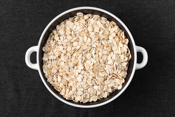 A lot of dry oatmeal lies in a plate on a dark background
