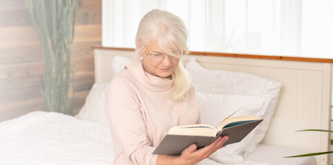 Senior woman reads, concentrated in a book.