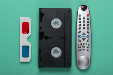 Anaglyph disposable paper 3d glasses, tv remote and video cassette on mint green background. Retro media, entertainment 80s. Top view