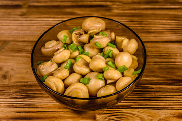 Glass bowl with canned mushrooms and green onion on wooden table