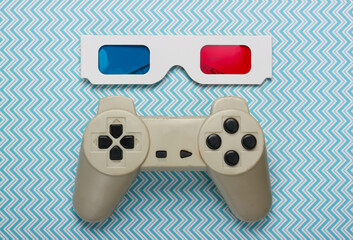 Anaglyph disposable paper 3d glasses and retro gamepad on blue background. Top view