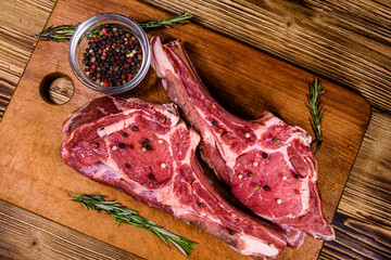 Raw ribeye steak, glass jar with spices and rosemary on cutting board. Top view