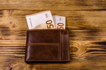 Brown leather wallet with fifty euro banknotes on the wooden background. Top view