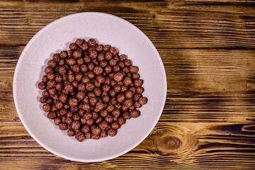 Ceramic plate with chocolate cereal balls on wooden table. Top view