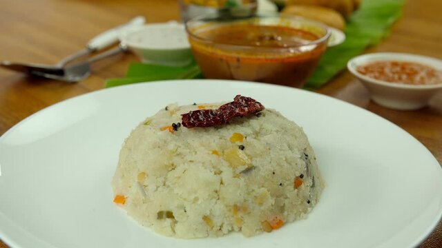 Popular South Indian vegetable Upma served in a ceramic white plate - food concept. Closeup shot of woman hands garnishing South Indian breakfast Upma with fried red chilly and curry leaf