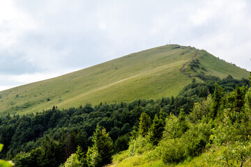 Mountain landscape with high green peak and blue sky with clouds. Walk in summer mountains