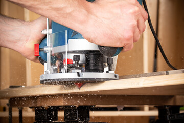 closeup of carpenter with hand wood router machine at work. closeup of routing bevel into plank of...