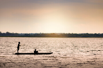 Fototapeta premium Silhouette image of two boys on a small boat for fishing in the evening.
