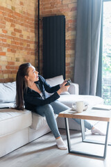 Fototapeta na wymiar KYIV, UKRAINE - APRIL 29, 2020: happy young woman holding joystick while playing video game in living room