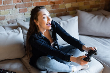 KYIV, UKRAINE - APRIL 29, 2020: excited woman holding joystick while playing video game in living room