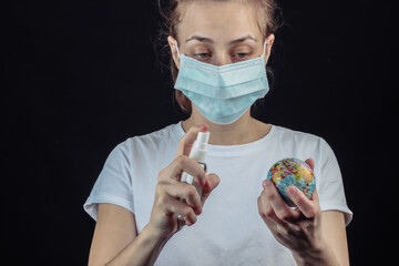Woman in a median face mask holding globe and disinfects with antiseptic on a black background....