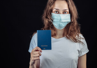 Traveling for the covid-19 pandemic. Woman in a medical mask holds a passport on a black background.