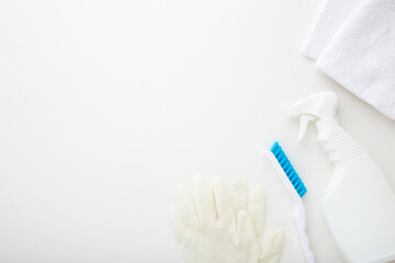 White bottle, towels, rubber protective gloves and brush. Cleaning set for different surfaces in kitchen, bathroom and other rooms. Light gray background. Top down view. Empty place for text or logo.
