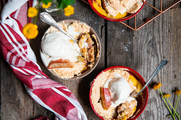 Top view of homemade portion desserts with rhubarb-strawberry puree, vanilla custard, shortcrust dough with baked meringue in ceramic forms and yellow flowers on brown  paper on wooden table.