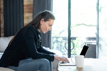 side view of happy freelancer using laptop with blank screen near cup on coffee table