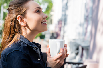 side view of cheerful woman holding cup of coffee outside