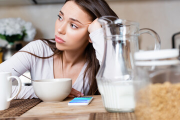 selective focus of sad girl near bowl, jug, cup and smartphone with booking app