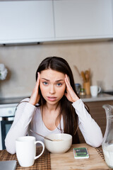 Obraz na płótnie Canvas upset girl touching head near bowl, jug and smartphone with booking app