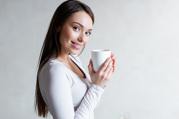 cheerful girl holding cup of tea and smiling at home