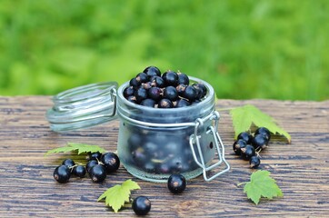 Black currant in a glass jar on a wooden table, against a background of nature. Eco-friendly...