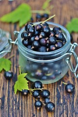 Black currant in a glass jar on a wooden table, against a background of nature. Eco-friendly...