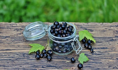 Black currant in a glass jar on a wooden table, against a background of nature. Eco-friendly...