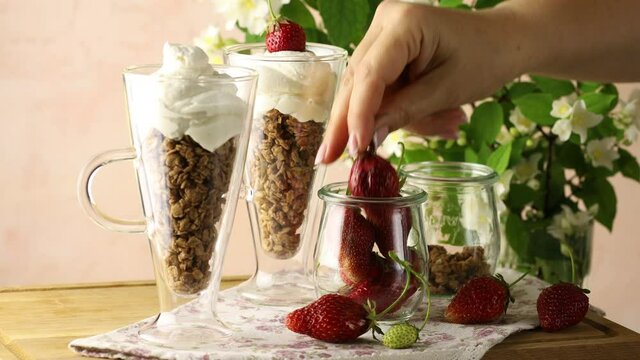 Woman hand decorated healthy breakfast with granola and greek yogurt fresh raw strawberry.