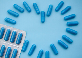 Blue capsules on a blue background. Flatlay, layout, copyspace. blister with blue capsules . capsules are arranged in the form of a heart