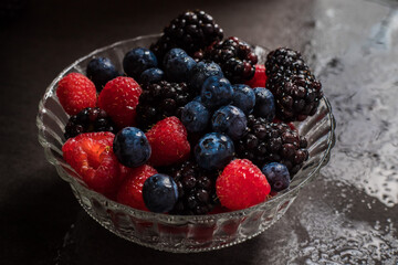 close up of wet raspberry, blueberries and blackberries in a glass bowl 