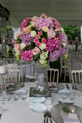 A luxury alfresco wedding reception set up at the countryside; white rustic tiffany chairs, top table flower arrangements, crystal center pieces, tableware and cutlery
