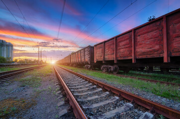 Fototapeta na wymiar Railway station with freight trains at colorful sunset. Railroad in summer. Heavy industry. Industrial landscape with train, green grass, railway platform, blue sky with pink clouds. Transportation