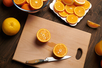 Fresh orange fruit whole and sliced on a wooden table, cutting board and kitchen knife. A plate full of citrus slices - natural and healthy food. Glass of fruit cocktail.