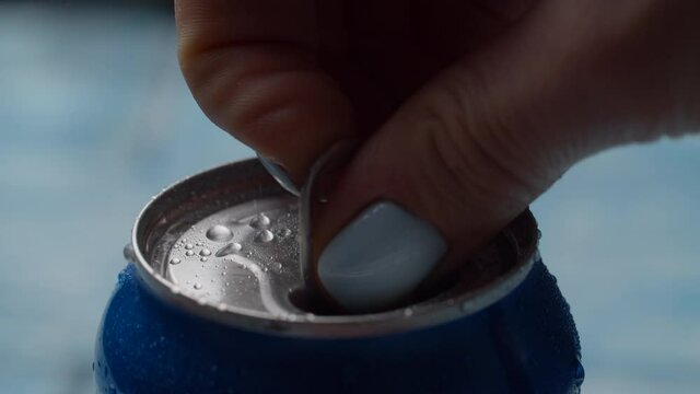 Close up of female hand opening wet blue soda can on bright background in slow motion. Blue cola can opening.