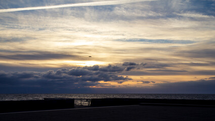 A single bird is flying across the dramatic sky after a storm as the sun sets over the sea Oresund