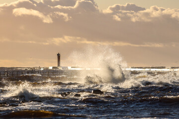 Late sunset view of old lighthouse pier and large storm waves.