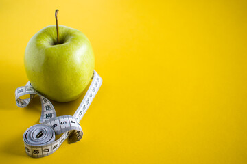 Green apple with white tape measure on yellow background. Healthy food concept