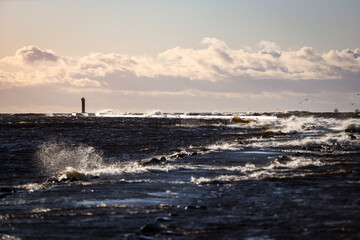 Windy late evening sunset view to Baltic sea lighthouse with large storm waves.