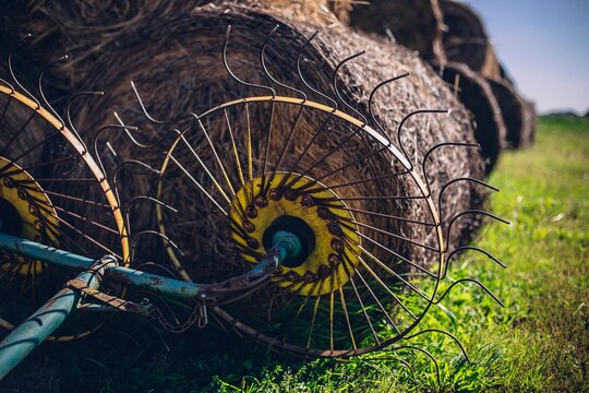 Closeup of a hay tedder with hay rolls  in the background on a field