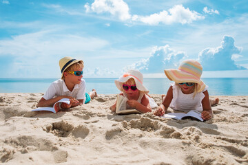 happy kids -boy and girls- read books on beach, summer reading on vacation