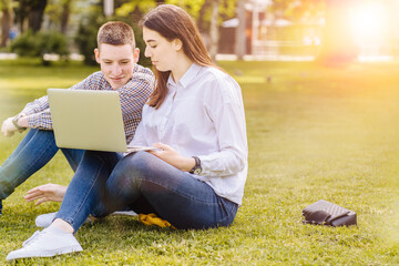 Multi ethnic couple of teenagers, millennial couple handsome man and woman sitting on the grass using laptop. People, communication, relations concept.