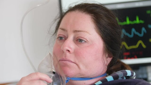 Sick woman puts on oxygen mask against background of monitor with vital indicators