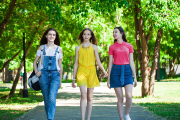 Three young women are walking in a summer park
