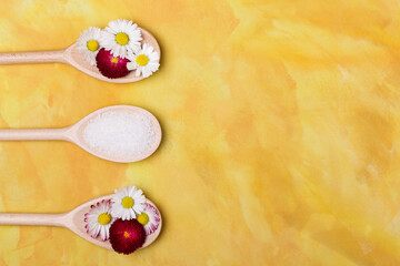 Spa background with spoons of salt and flowers. Flat lay overhead top view of wooden spoon with salt on yellow background.
