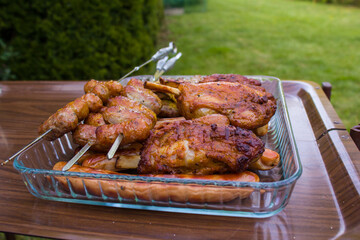 Freshly cooked meat in a glass tray on a brown table, barbecue in the garden.