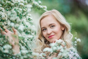 Portrait of a beautiful young blonde in white blossoms. Spring portrait of a young woman.