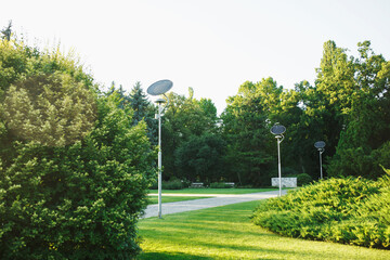 Compact solar panels setted on street lanterns in green lush city park, no people