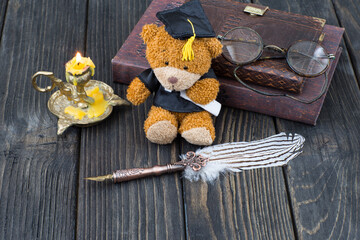 old fountain pen, candle in a candlestick, glasses, books and a bear graduate in a graduate cap